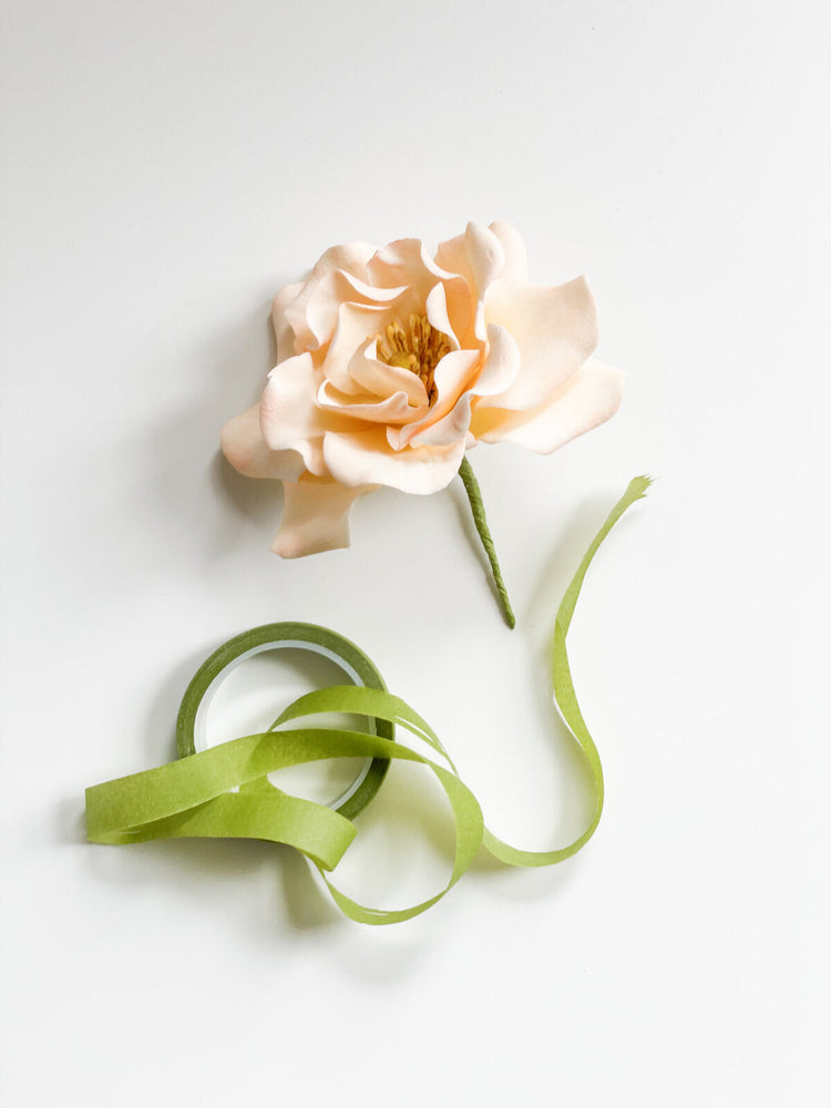 Light green floral tape next to an ivory sugar flower rose on a light gray background