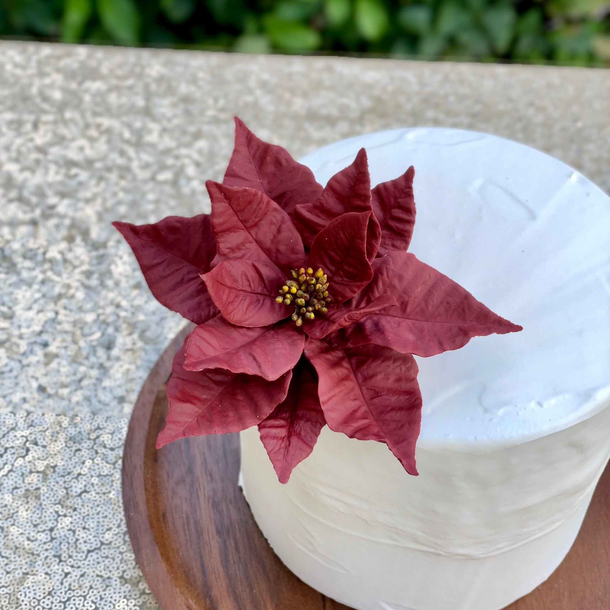 Burgundy Red poinsettia sugar flower on a white cake with a wooden base.
