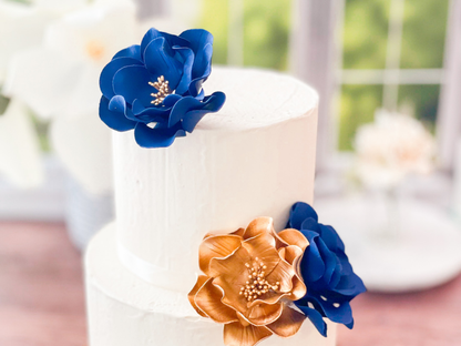 White wedding cake with navy blue and gold gumpaste floral decorations on a blurred background