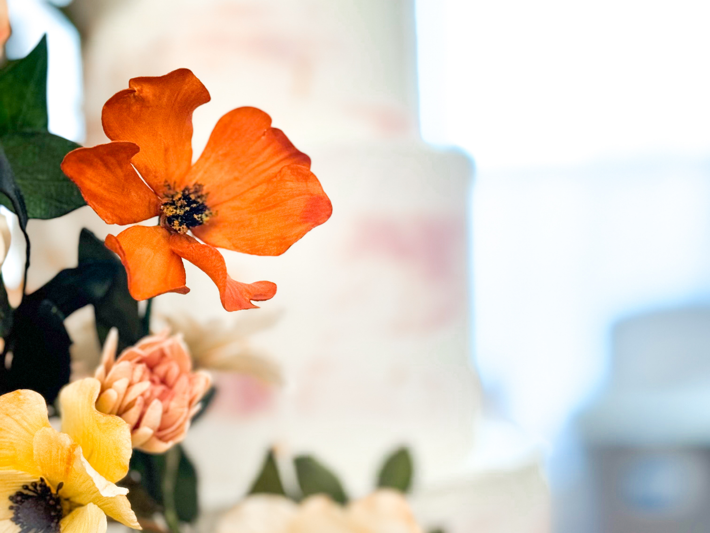 Close up of Handmade orange cosmos sugar flower with 3 inch diameter on a wedding cake with the background blurred