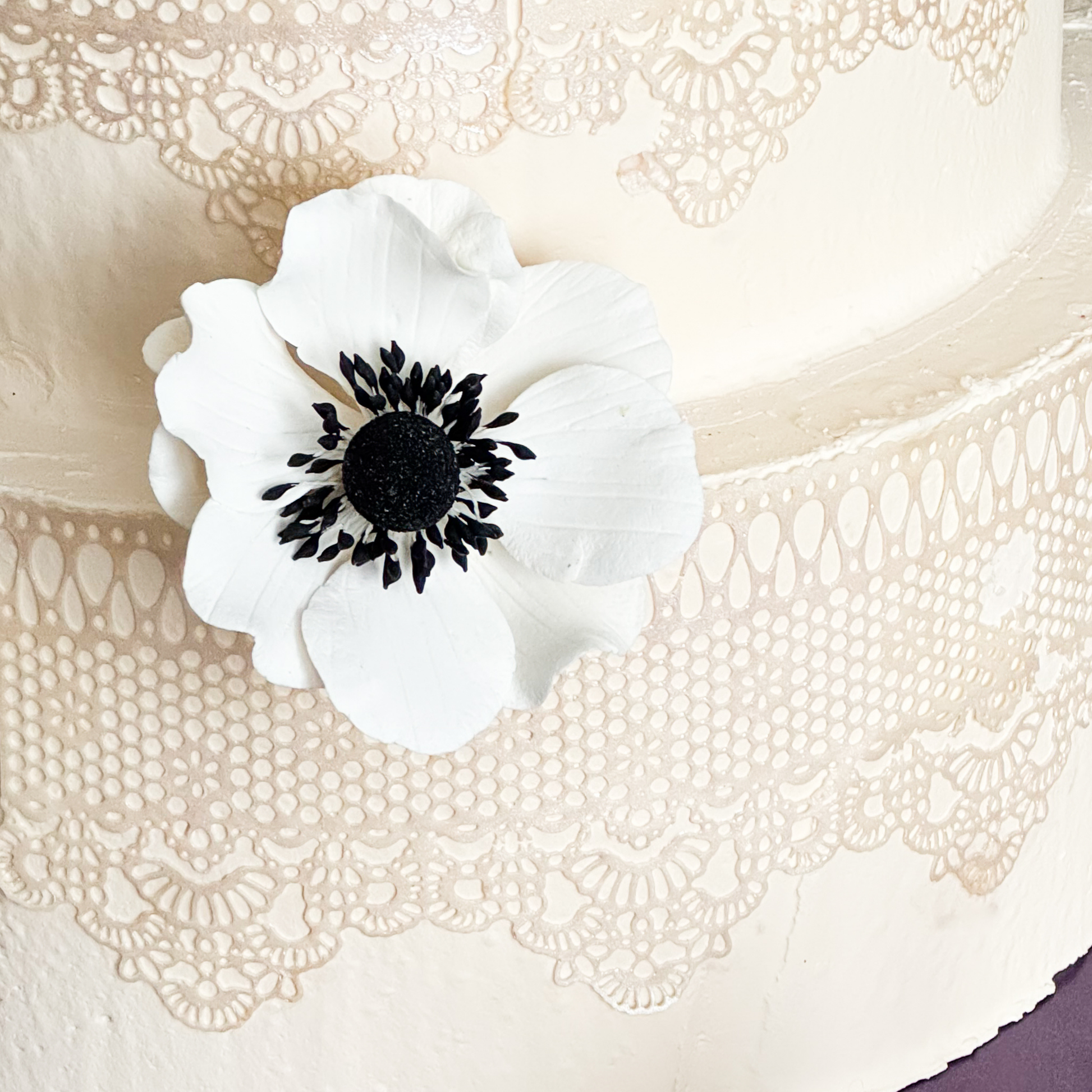 White Gumpaste flower with black center on a textured white wedding cake