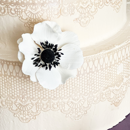 White Gumpaste flower with black center on a textured white wedding cake
