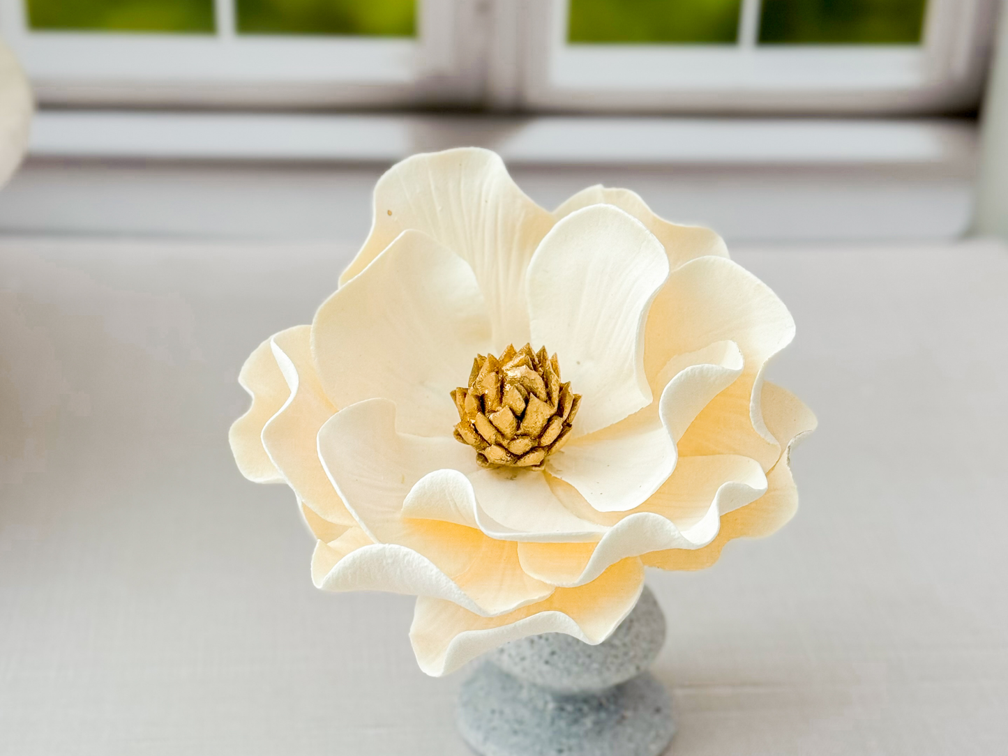 Ivory and gold sugar flower on a gray pedestal against a blurred window background