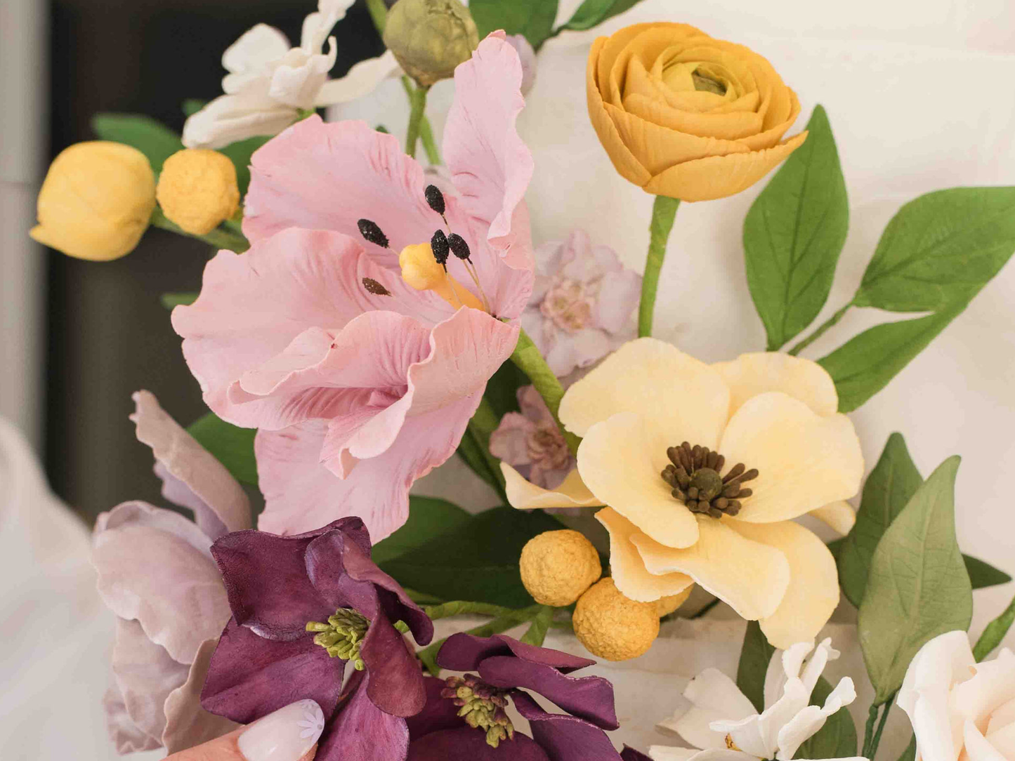 Colorful floral arrangement with a focus on pink, yellow, and purple flowers on a white wedding cake