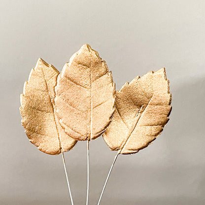 Three Golg gumpaste leaves on floral wire against a neutral background